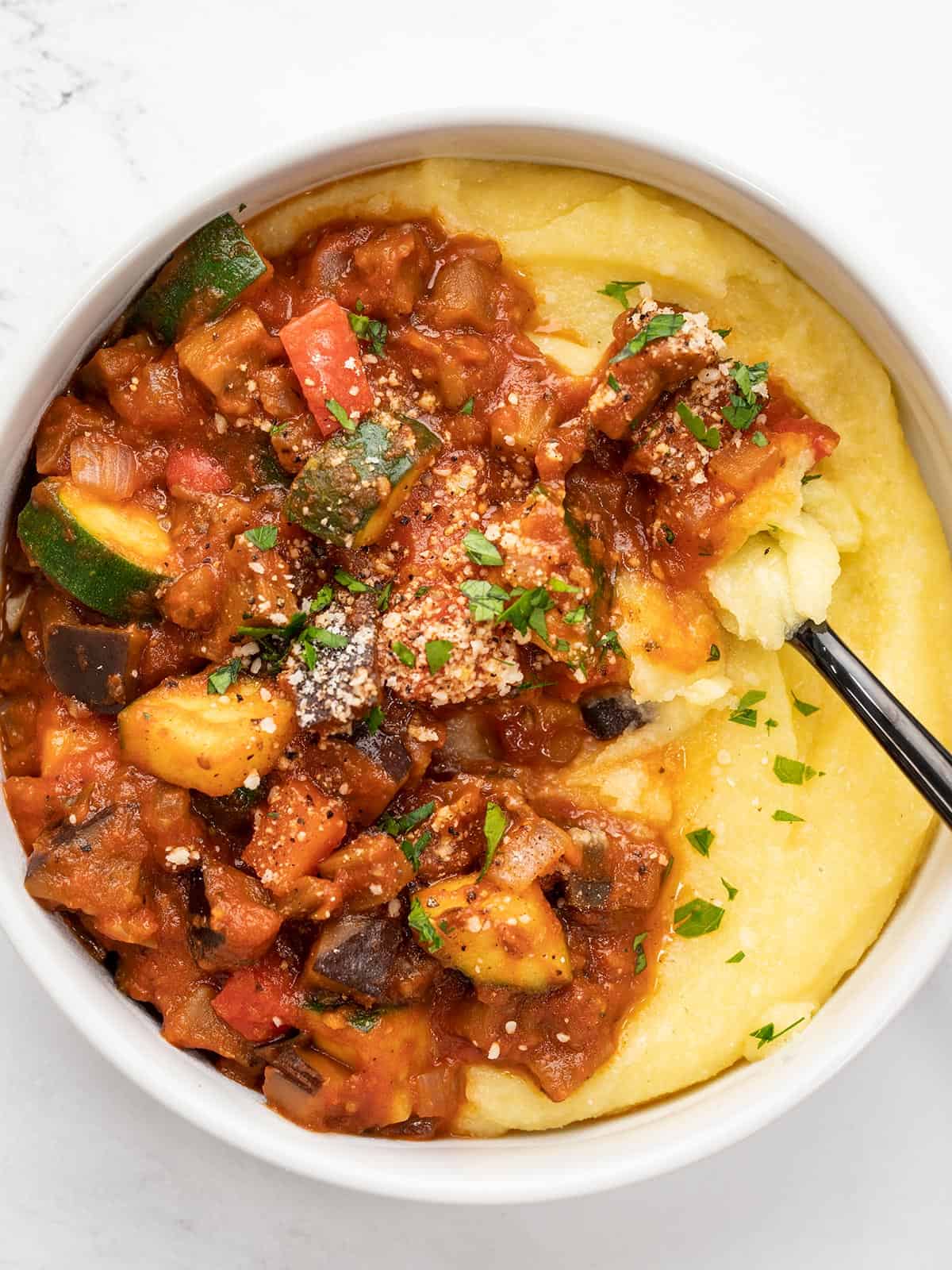 Close up overhead view of vegetables in red sauce over polenta with a fork.