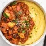 Close up overhead view of cornmeal and vegetables in red sauce in a bowl with a fork on the side.