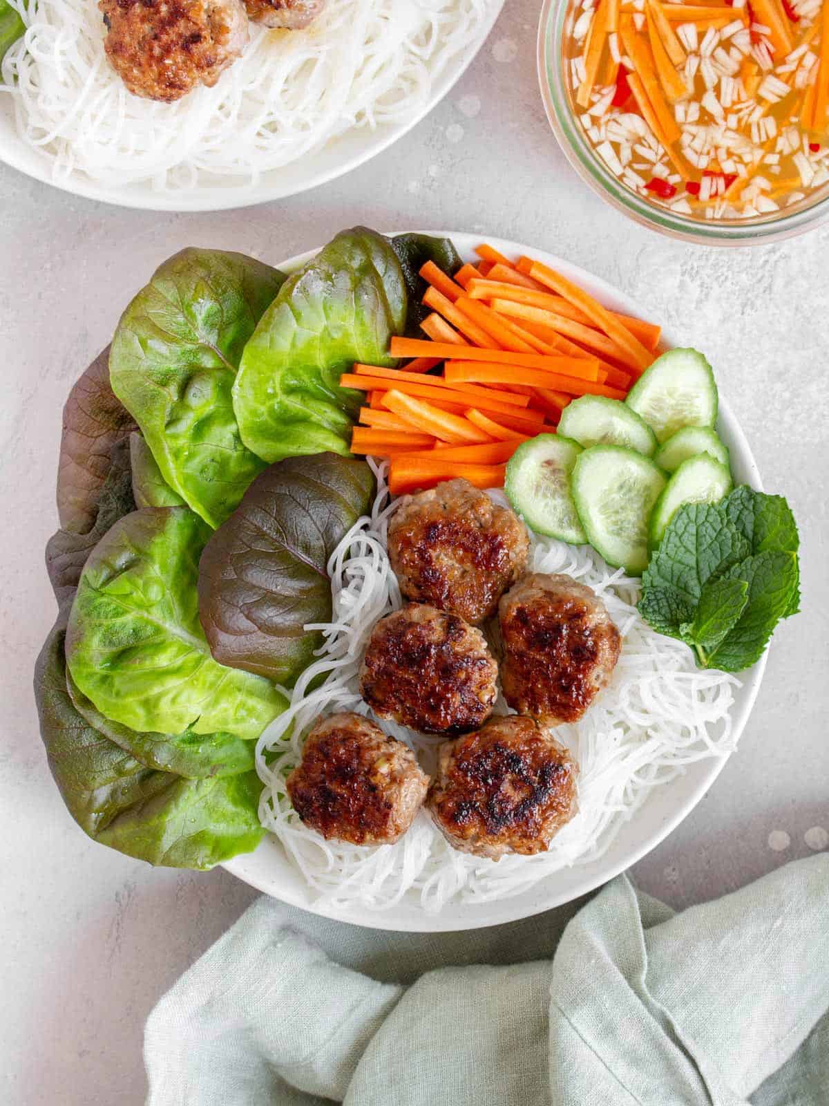 Overhead view of Bún chả in a bowl with noodles and vegetables, dipping sauce on the side.