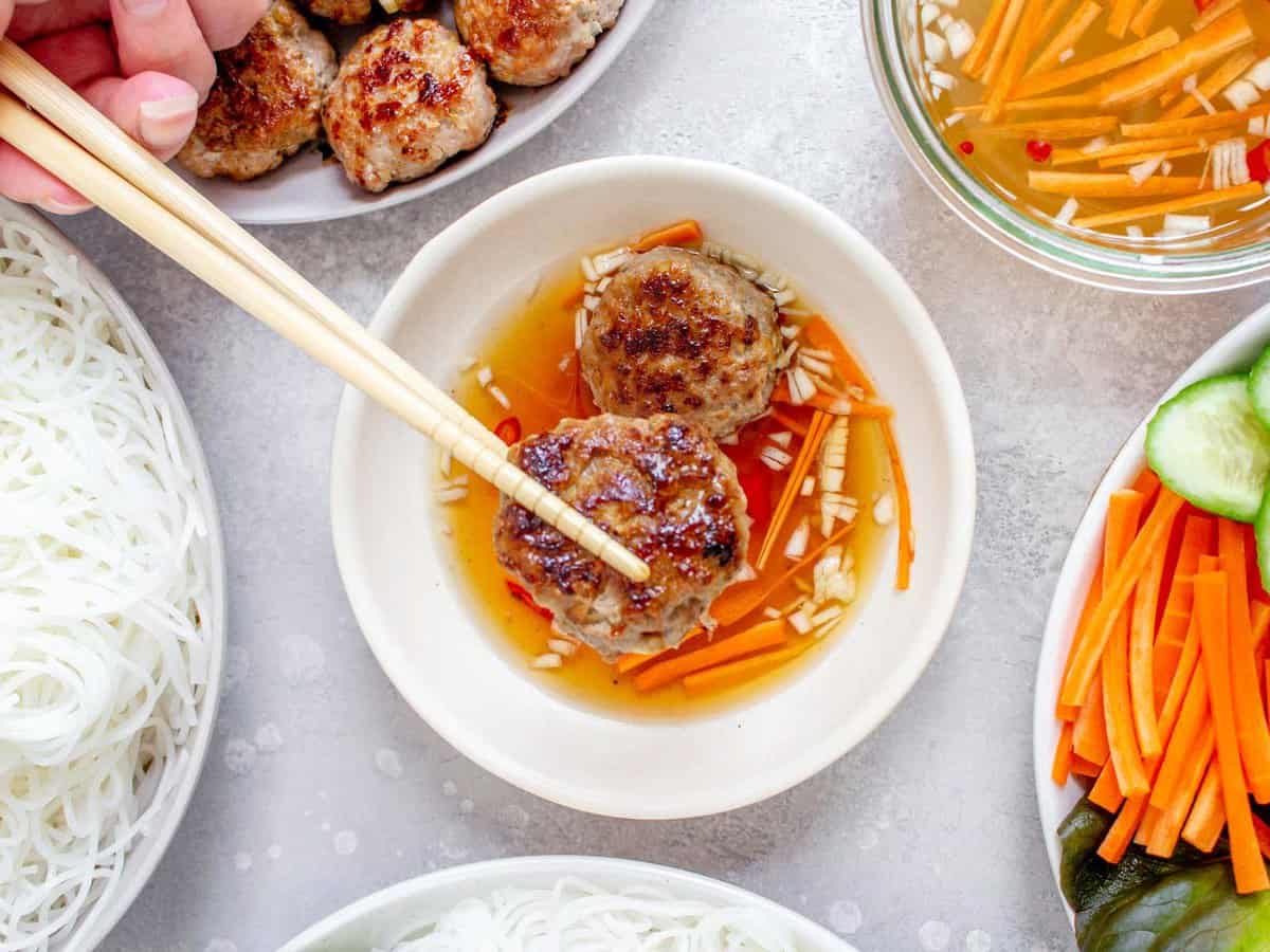 Bún chả being dipped in a bowl of sauce with ingredients on the sides.