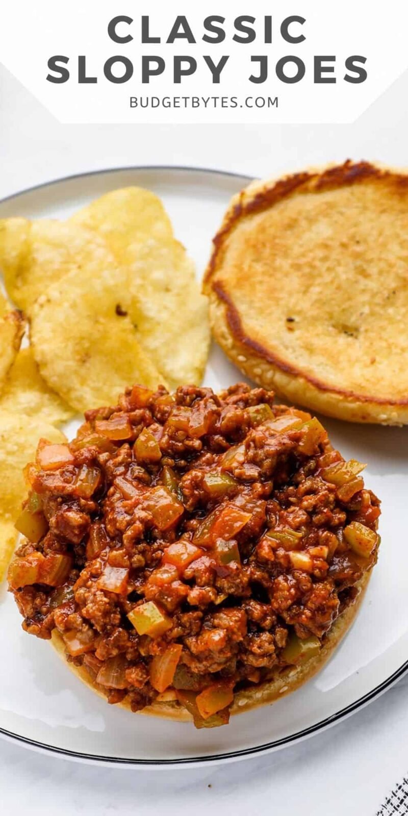 An open-faced sloppy joe on a plate with chips.