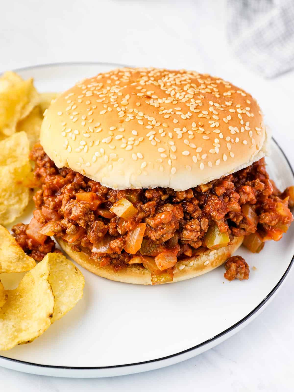Side view of a sloppy joe on a plate with potato chips.