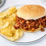 A sloppy joe on a plate with potato chips.