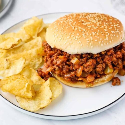 A sloppy joe on a plate with potato chips.