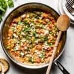 A skillet full of menemen with dishes and bread on the side.