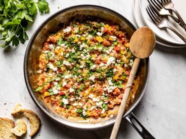 A skillet full of menemen with dishes and bread on the side.