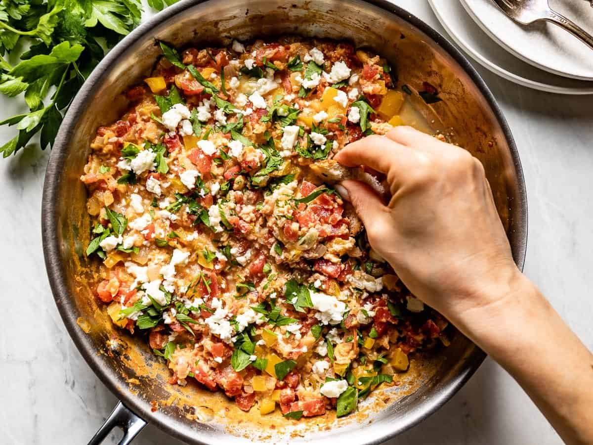 A hand dipping bread into a pan of menemen.