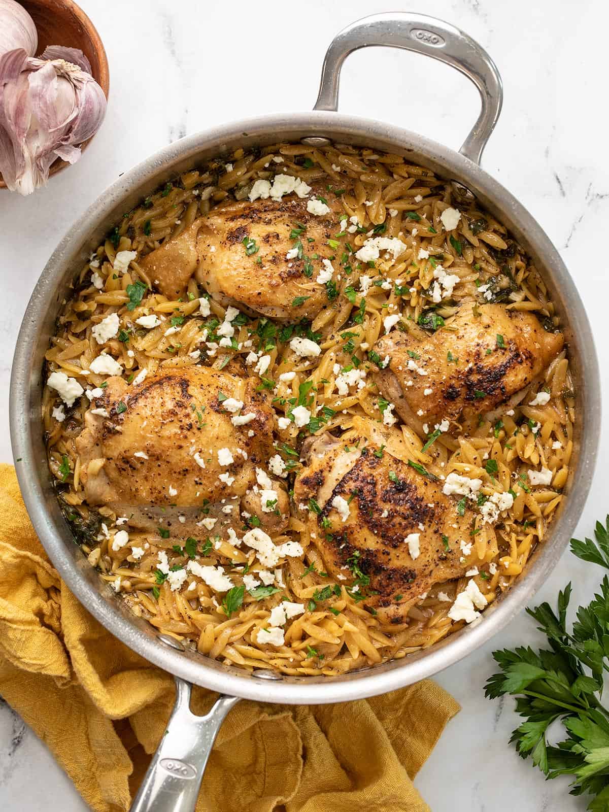 Overhead view of lemon pepper chicken and orzo in the skillet with a napkin and parsley on the sides.