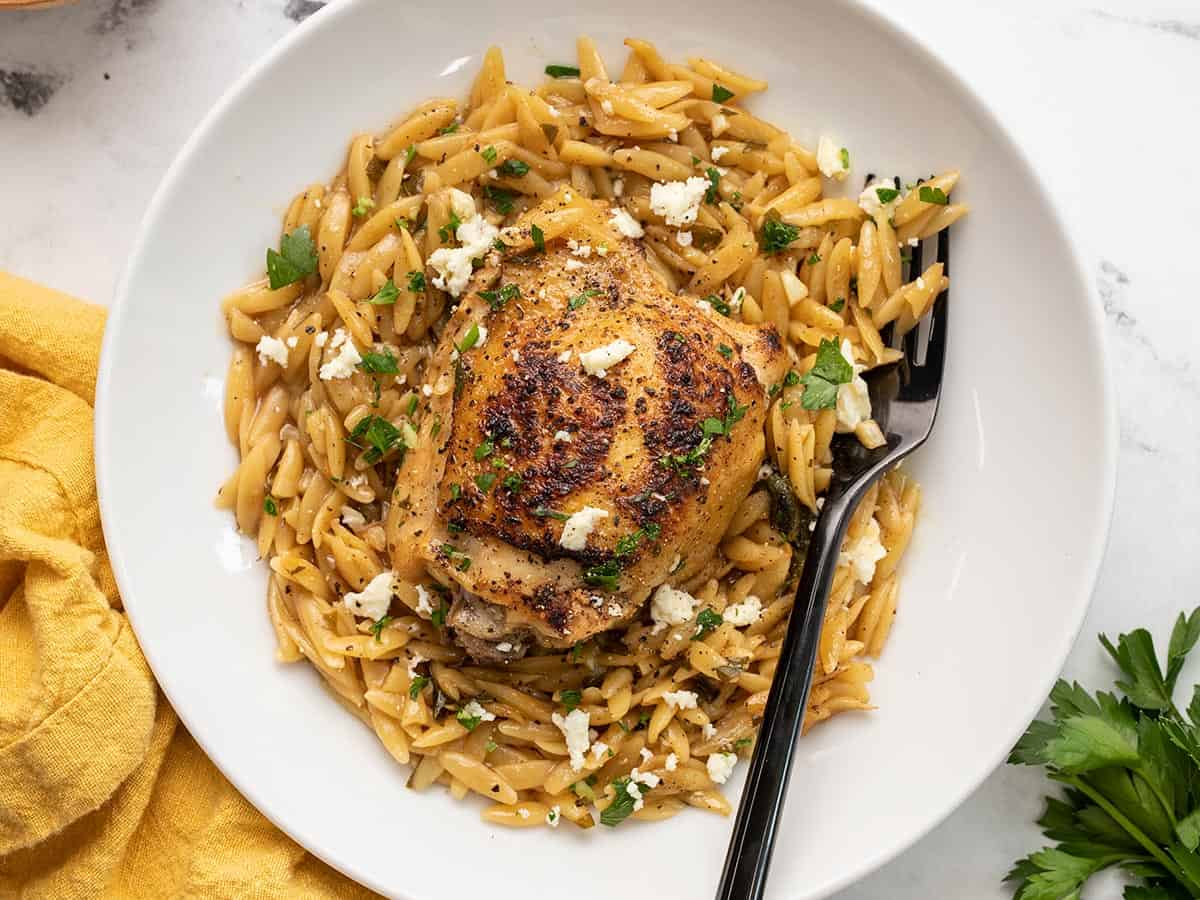 Lemon pepper chicken and orzo in a shallow bowl with a fork.