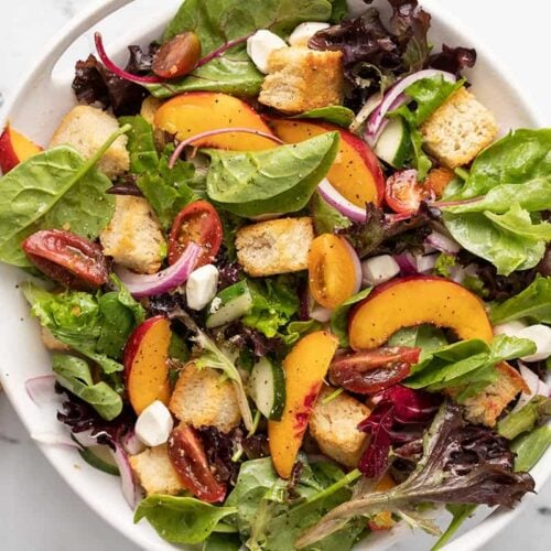 Overhead shot of panzanella salad in a white bowl with wood serving spoons next to it.