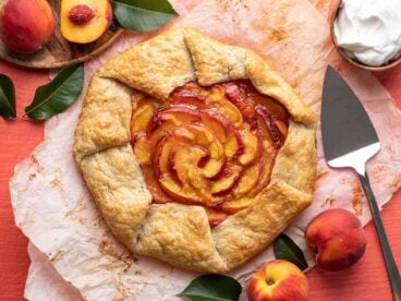 Overhead shot of peach galette surrounded by fresh peaches and leaves.