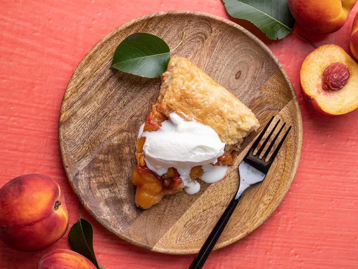 Overhead shot of slice of peach galette on a wood plate with a dollop of whipped cream.