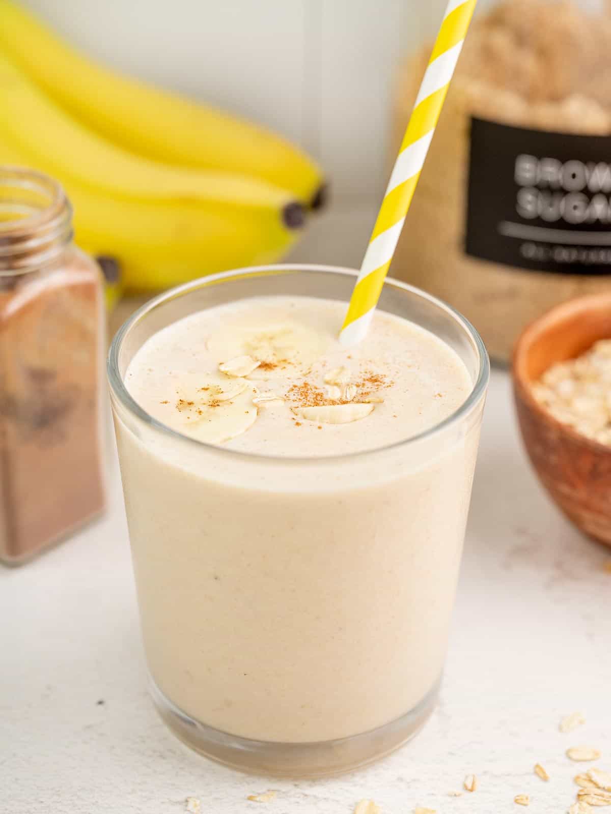 Peanut butter banana smoothie in a glass with a yellow striped straw.
