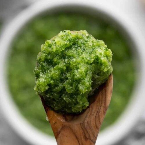 Close up of sofrito on a wooden spoon with the bowl in the background.