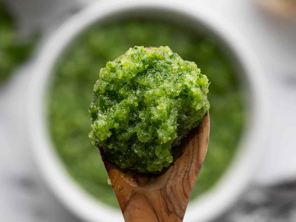 Close up of sofrito on a wooden spoon with the bowl in the background.