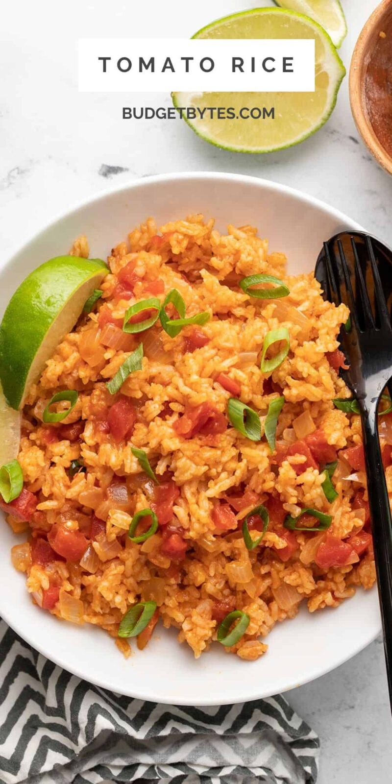 Overhead view of a bowl of tomato rice with lime and green onion.