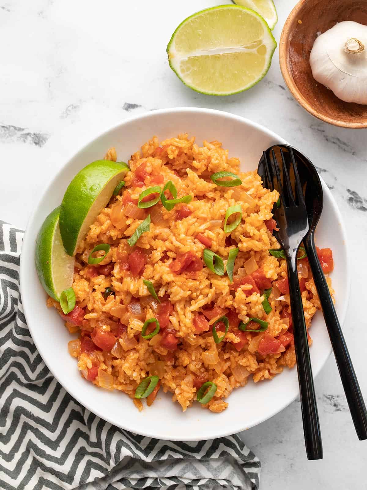 Tomato rice in a bowl with limes and green onion.