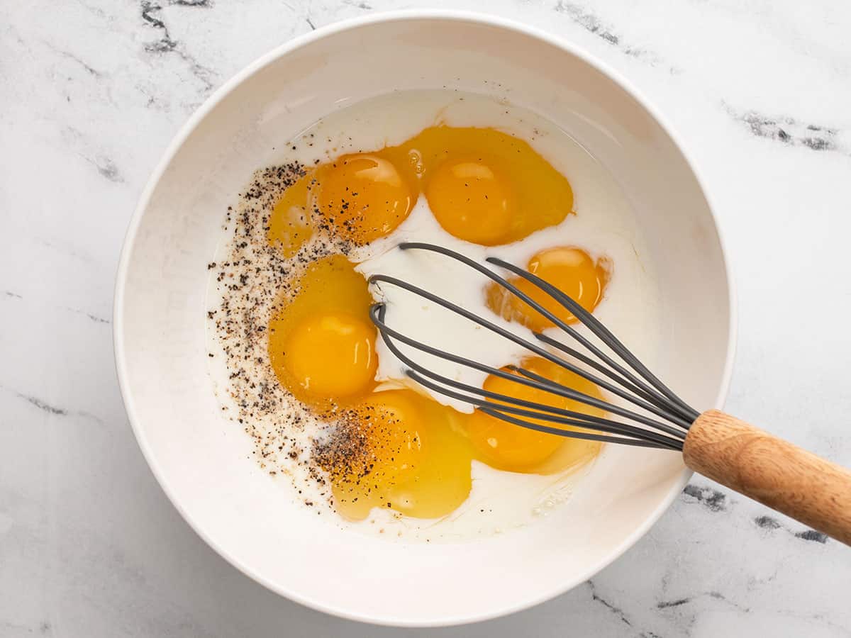 Eggs milk salt and pepper in a bowl with a whisk.