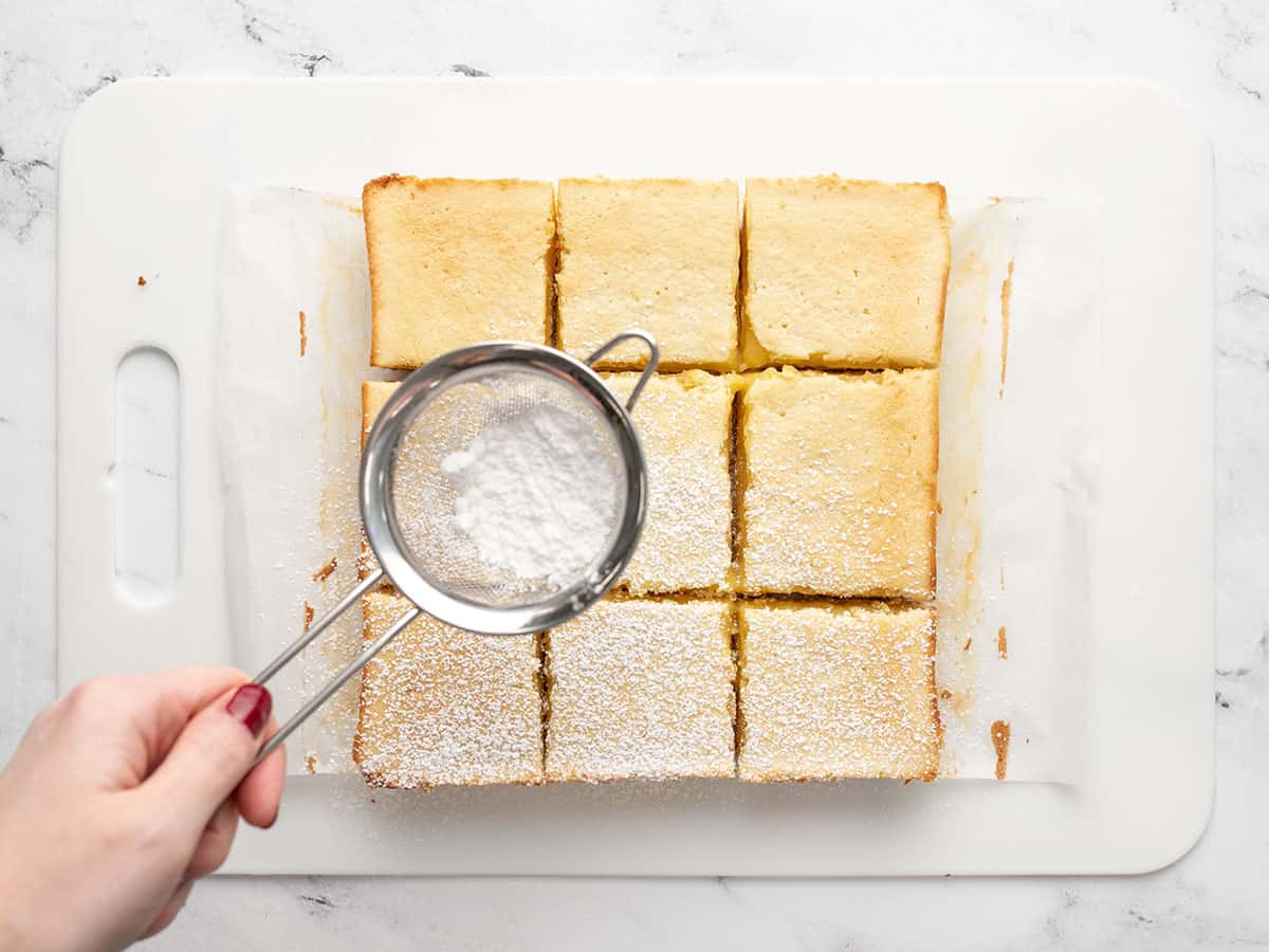 Powdered sugar being dusted onto sliced lemon bars.