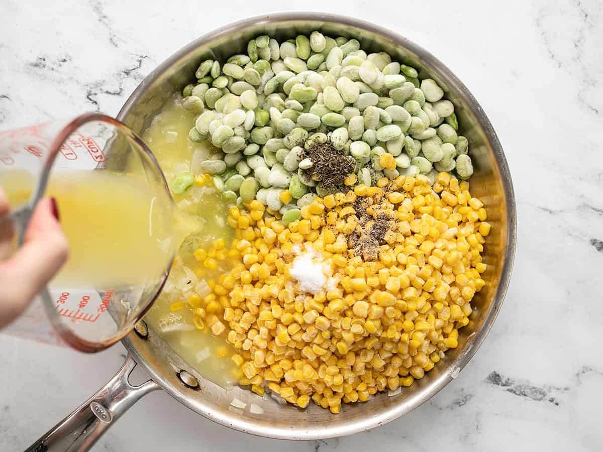 Corn, lima beans, spices, and broth being poured into the skillet.