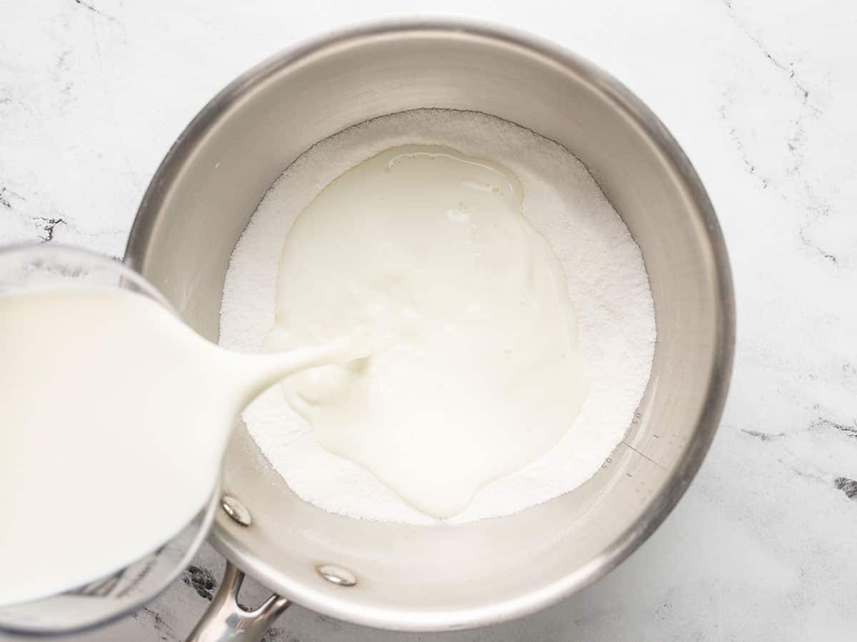 Overhead shot of milk being poured into dry ingredients in a pot.