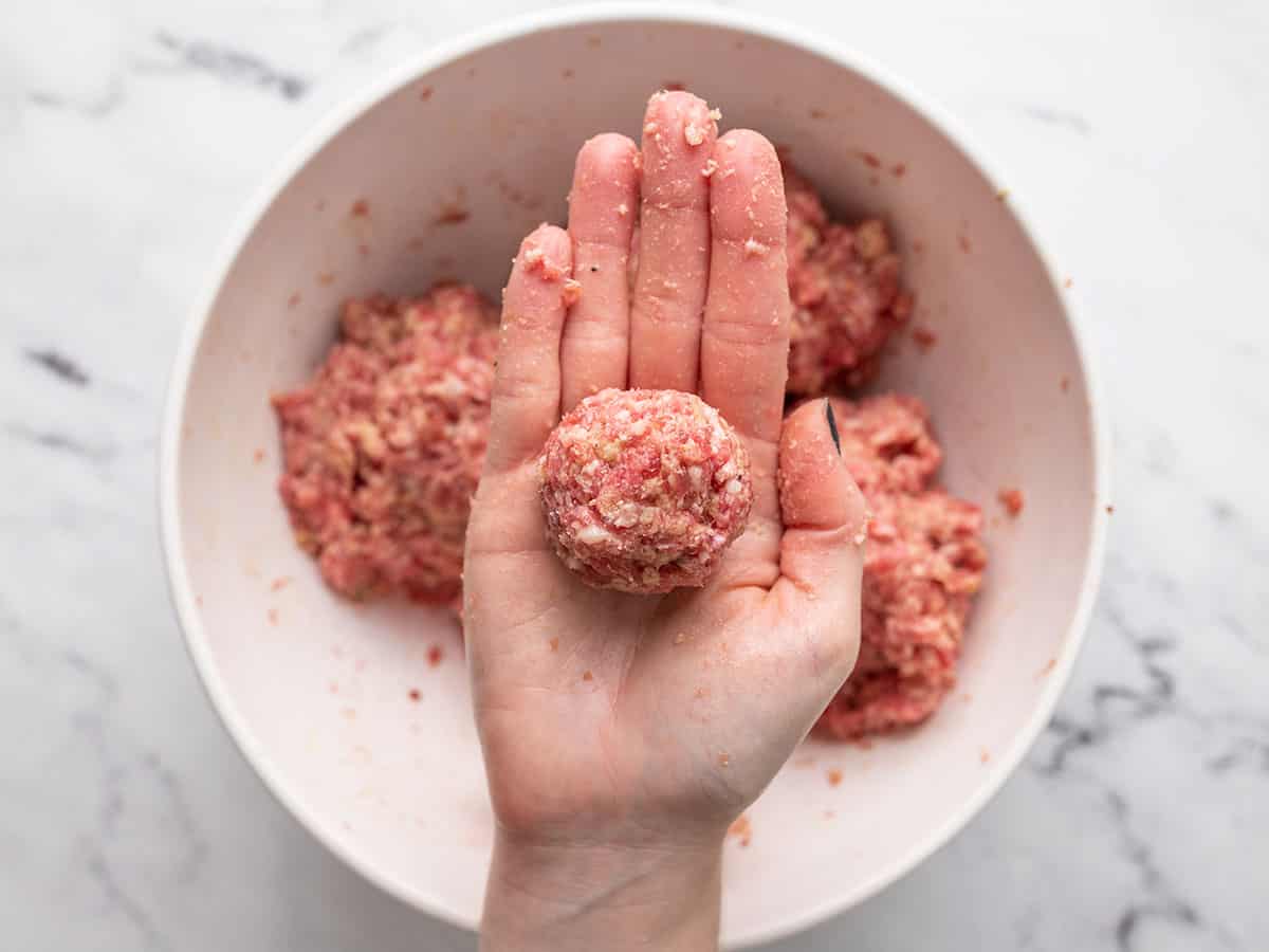 Shaped meatballs one held in a hand.