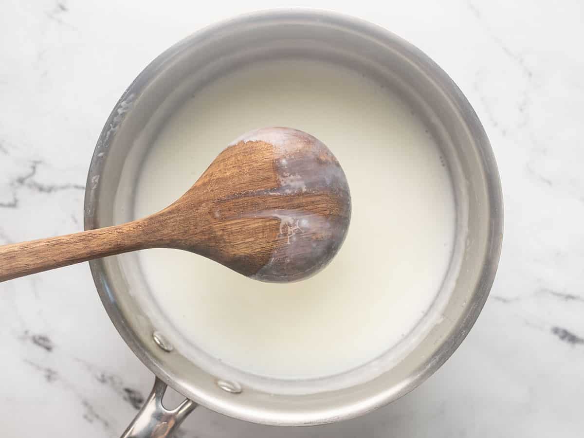 Overhead of a wooden spoon comin out of a pot with milk that has thickened on it.