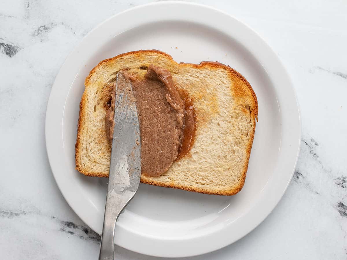Knife spreading cinnamon butter on slice of bread on a white plate.