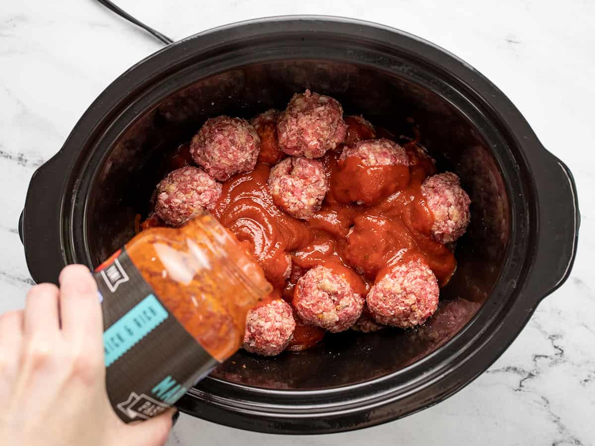Sauce being poured over the meatballs in the slow cooker.