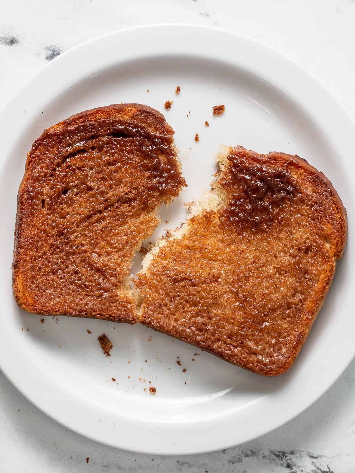 Overhead shot of cooked cinnamon toast ripped and served on a white plate.