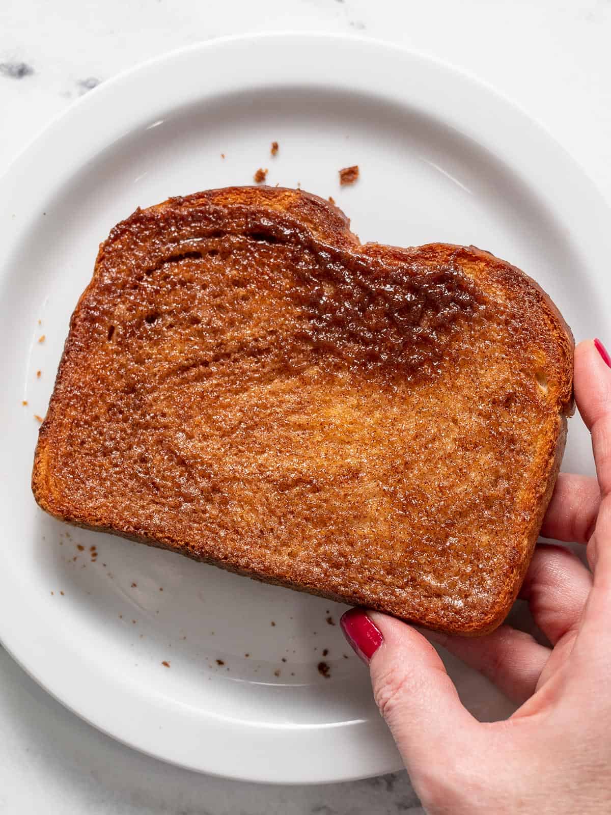 Overhead shot of hand holding cinnamon toast over a white plate.