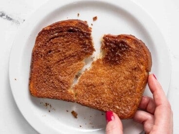 Overhead shot of hand holding cinnamon toast over a white plate.