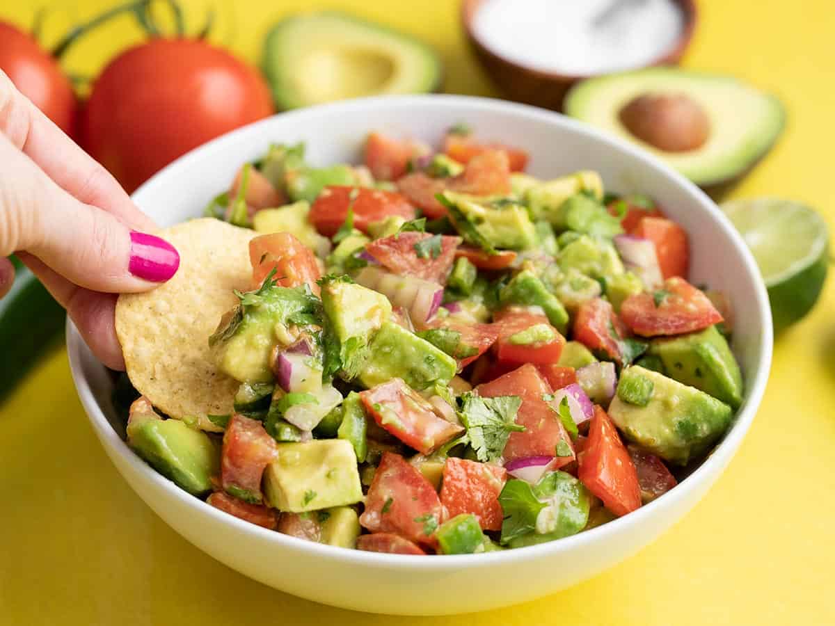A chip dipping into a bowl of avocado and tomato salad.