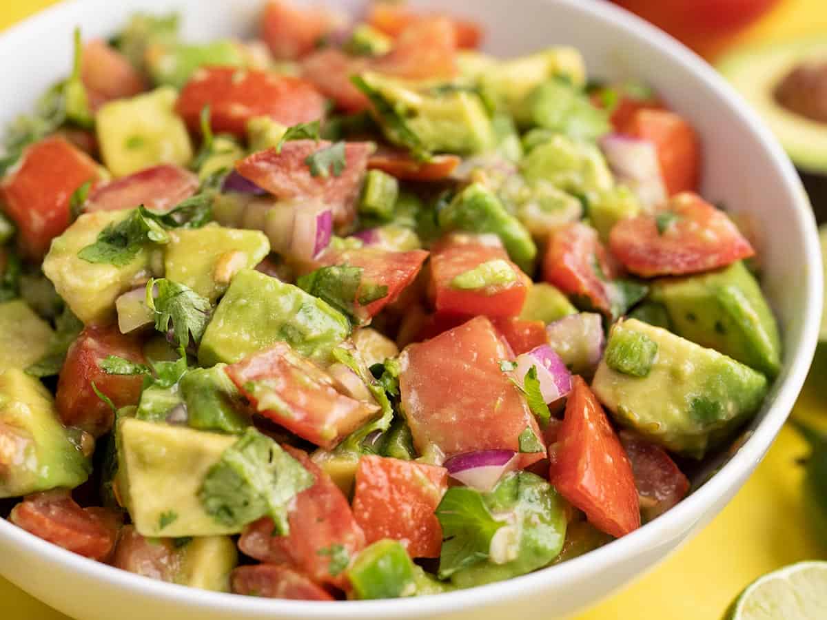 close up side view of a bowl full of avocado and tomato salad. 