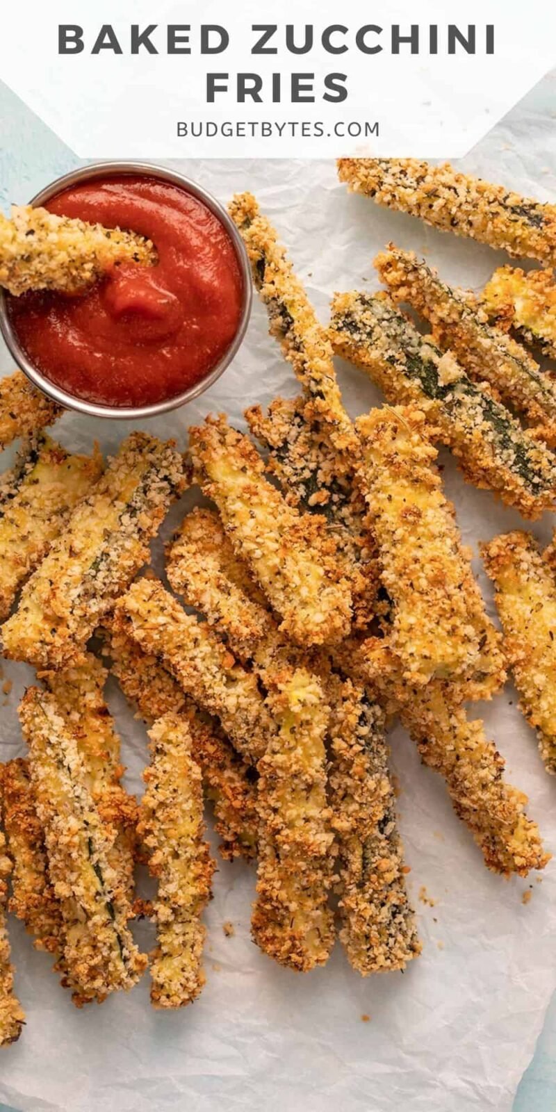 Baked Zucchini Fries on a piece of parchment with a dish of pizza sauce.