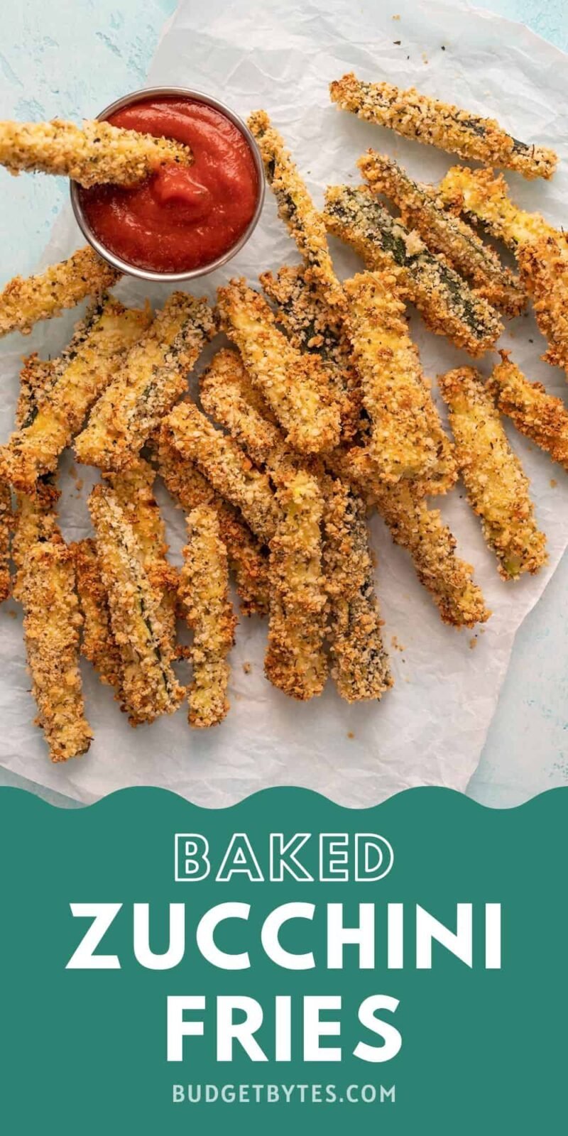 Baked zucchini fries on a piece of parchment with one dipped in a dish of pizza sauce.