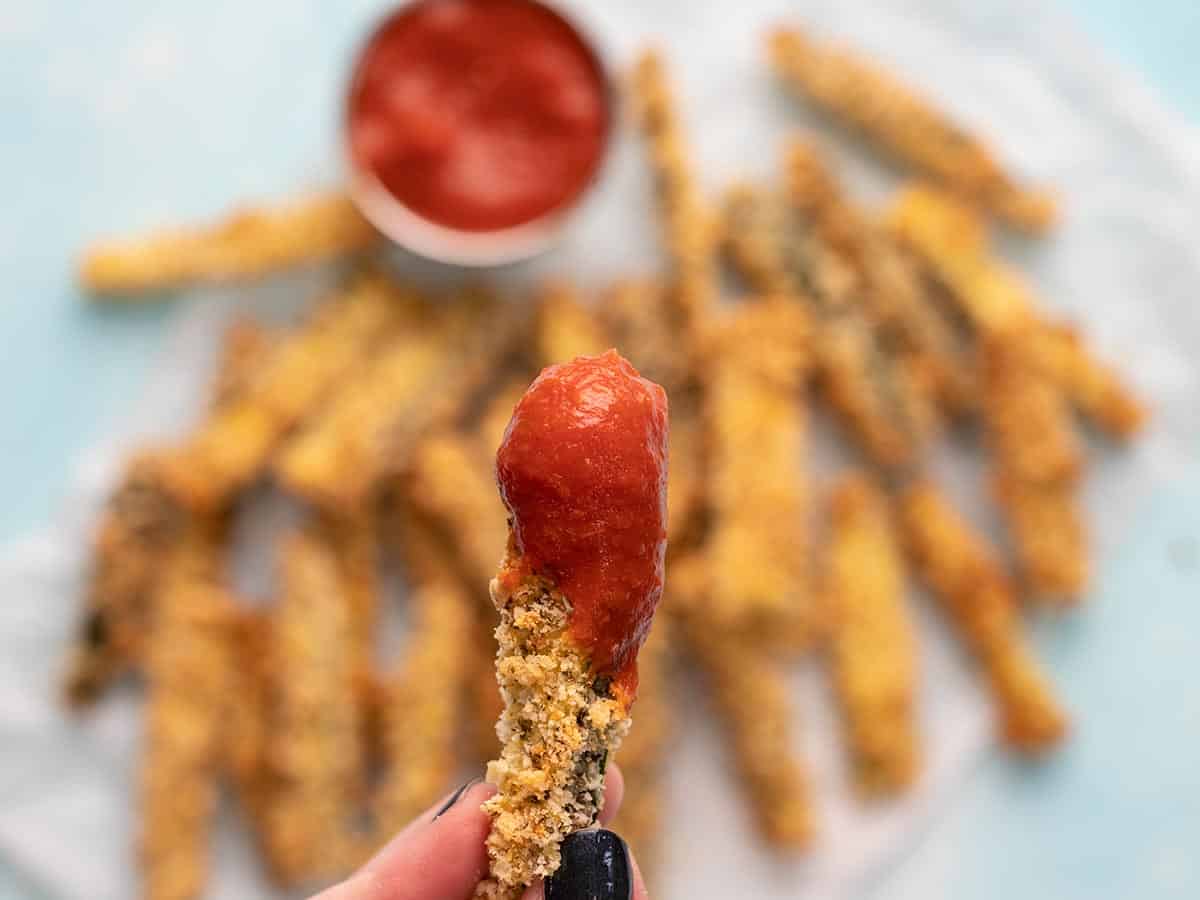 Close up of a zucchini fry dipped in pizza sauce.