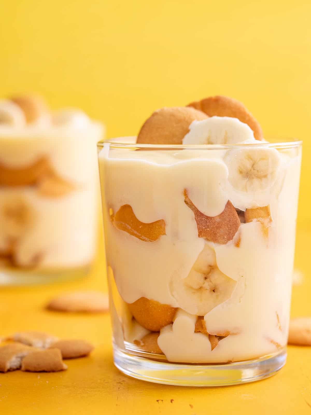 Side shot of banana pudding in a glass with a second glass in the background.