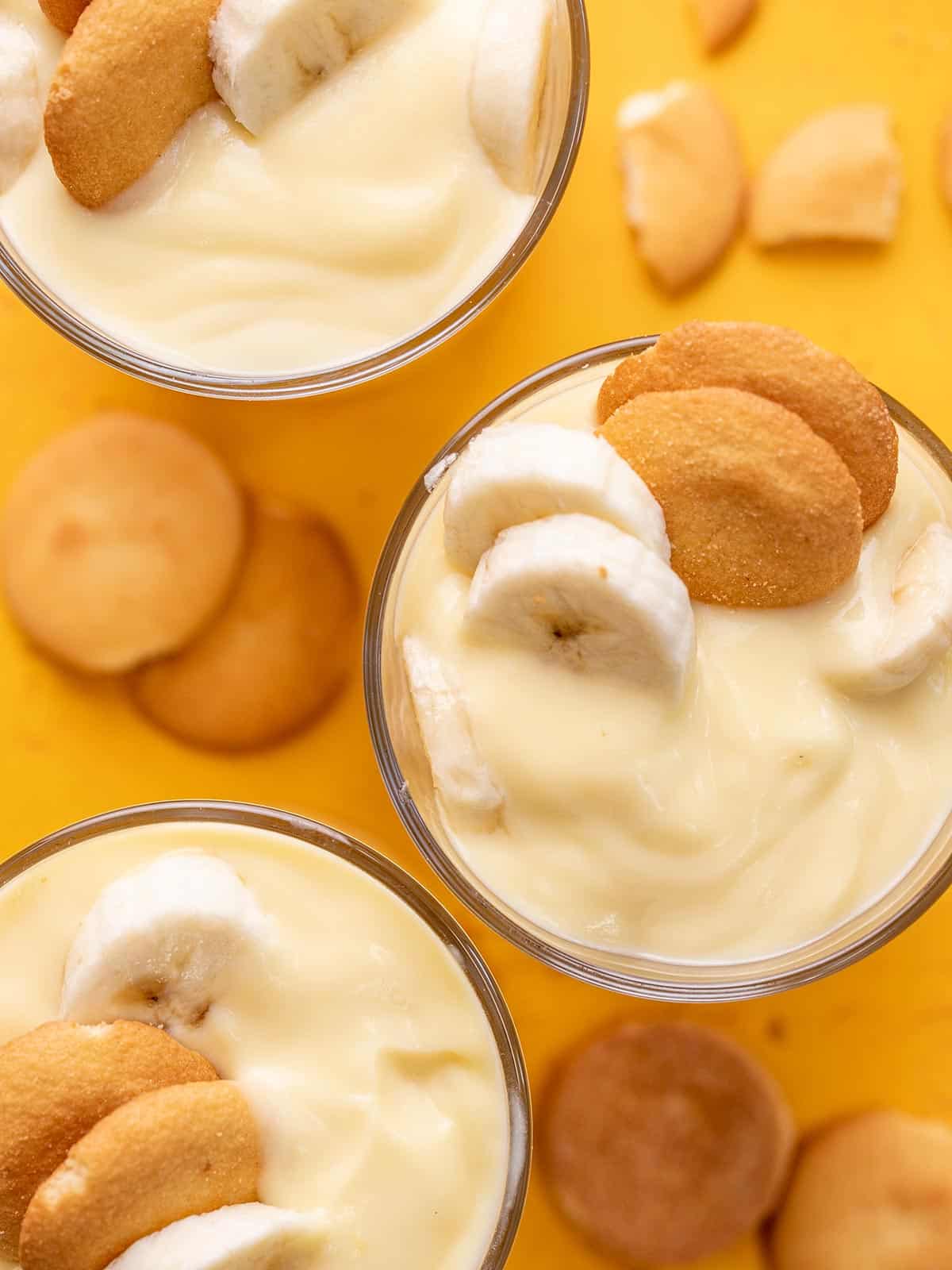 Overhead shot of three glasses filled with banana pudding with vanilla wafers next tot hem.