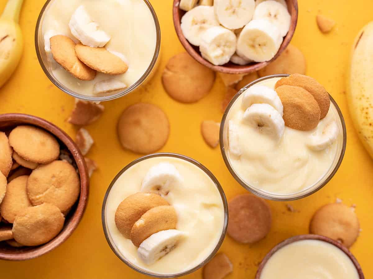 Overhead shot of three glasses of banana pudding with wafers on the counter and in a bowl.