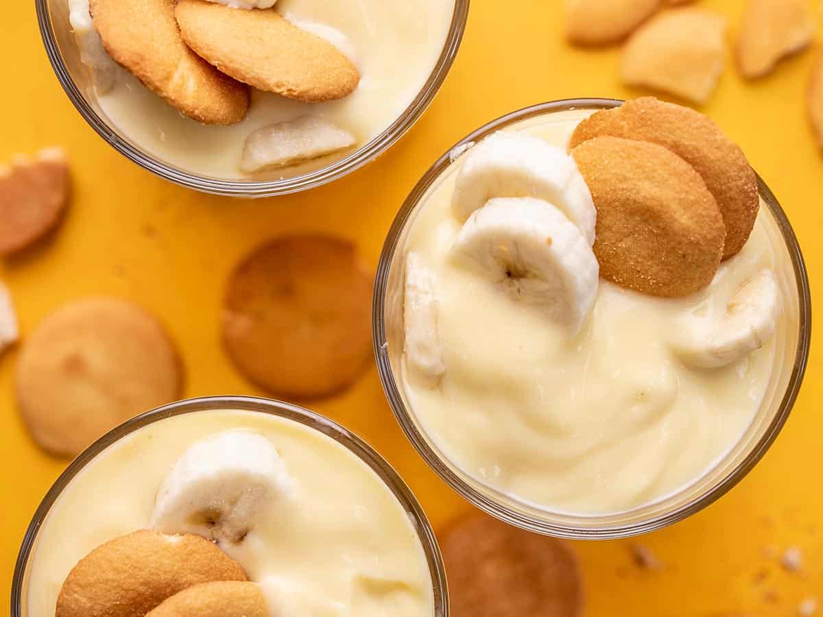 Overhead shot of banana pudding in three glasses with wafers scattered on the counter.