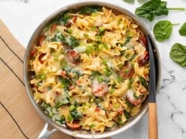 Overhead view of cheesy sausage pasta in the skillet with a spatula.