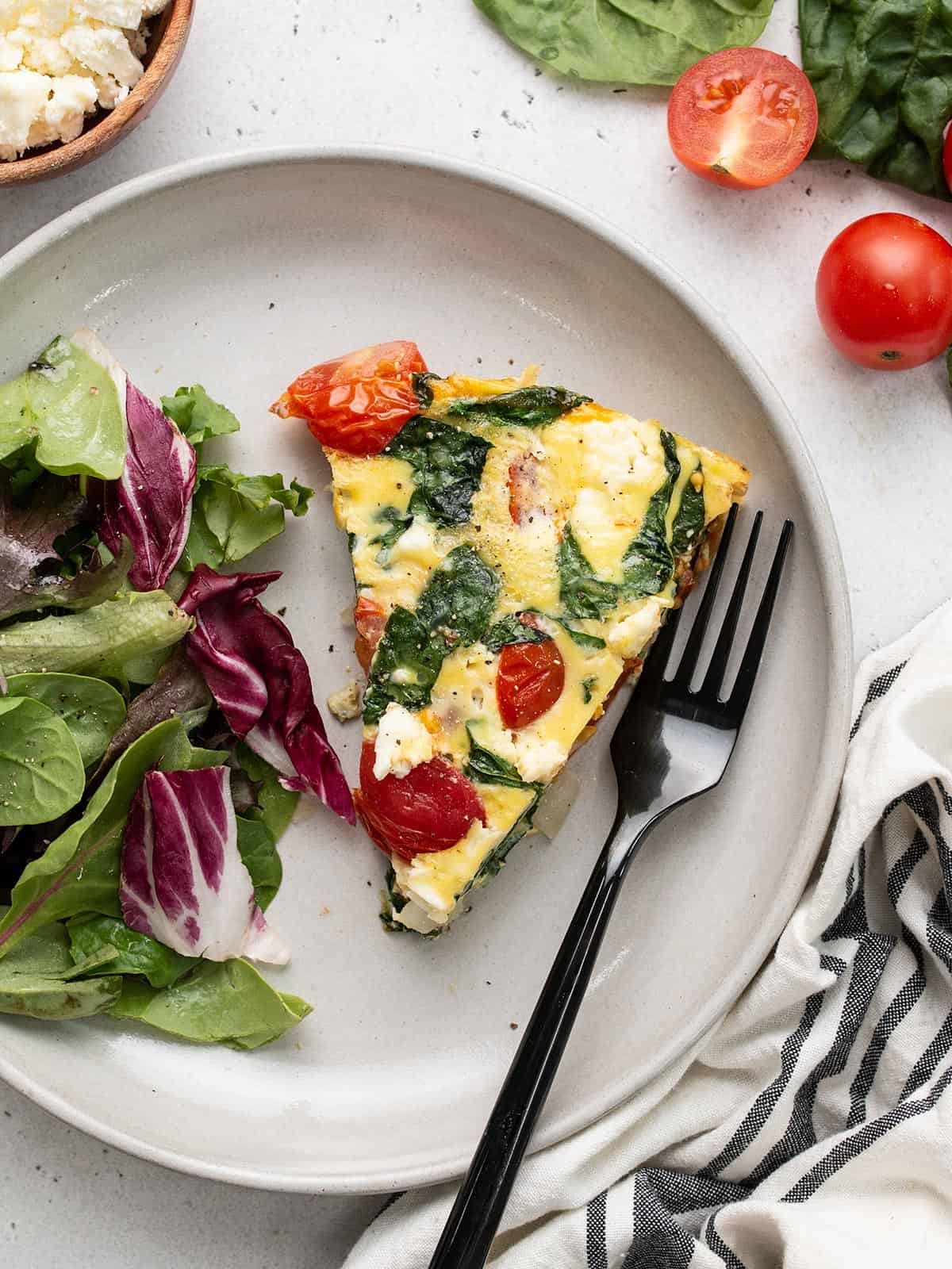A slice of frittata on a plate with a simple side salad.