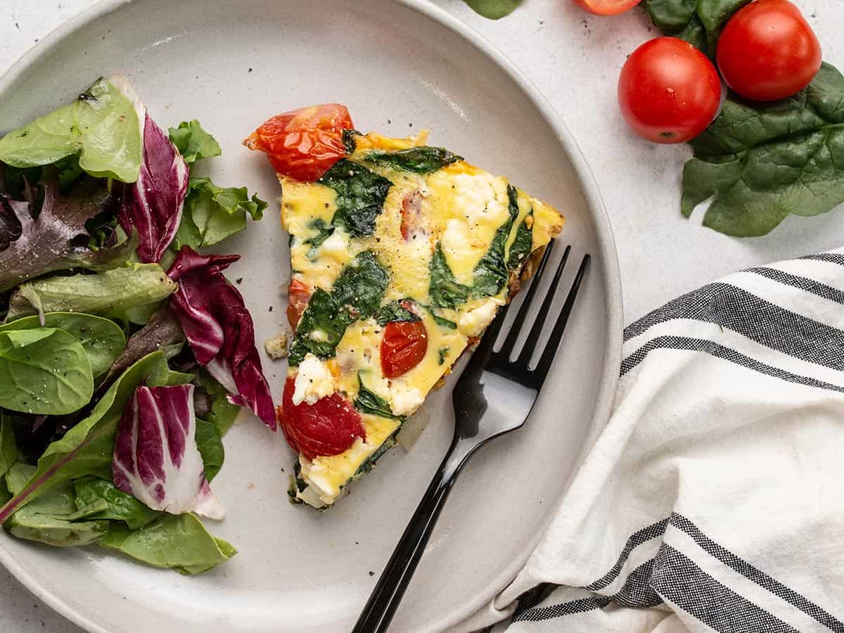 A slice of frittata on a plate with a side salad.