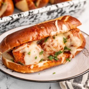 Side view of a meatball sub on a plate with the baking dish in the background.