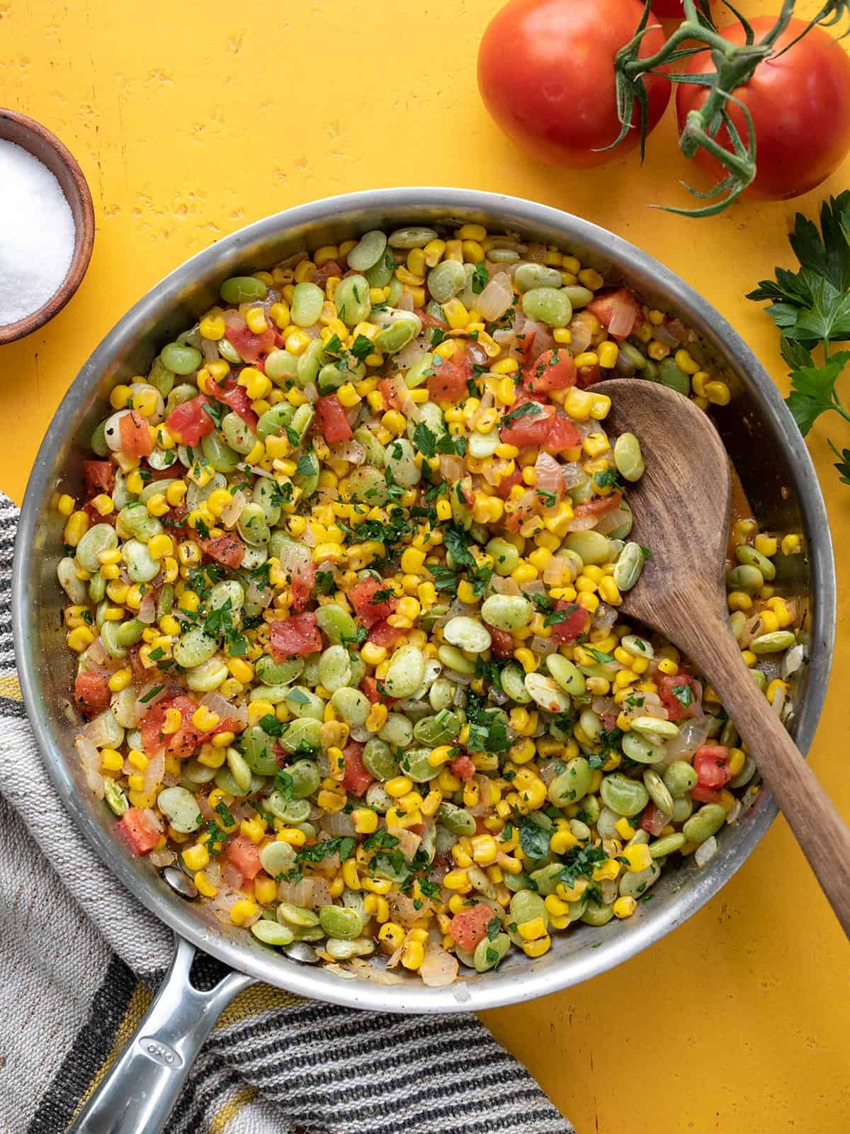 Succotash in a skillet with a wooden spoon, garnished with parsley.