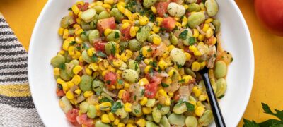 Overhead view of a bowl of succotash with a black spoon.