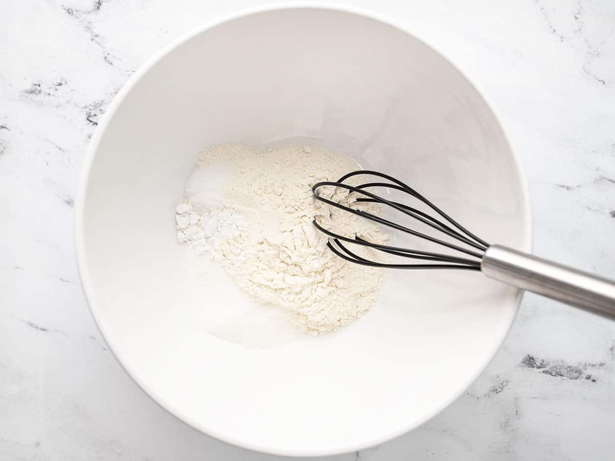 Overhead shot of dry ingredients and a whisk in a white bowl.