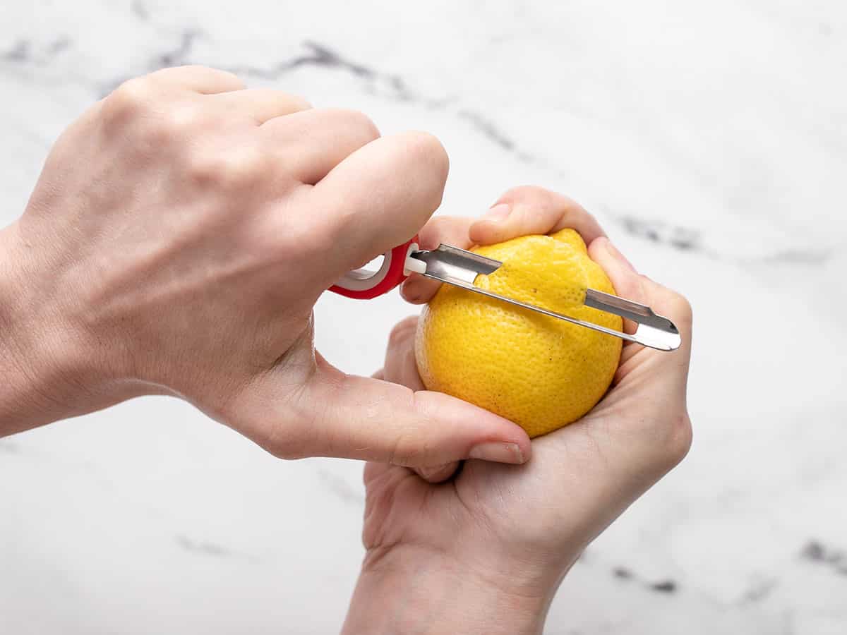 Overhead shot of a hand holding a lemon while a second hand zests it.