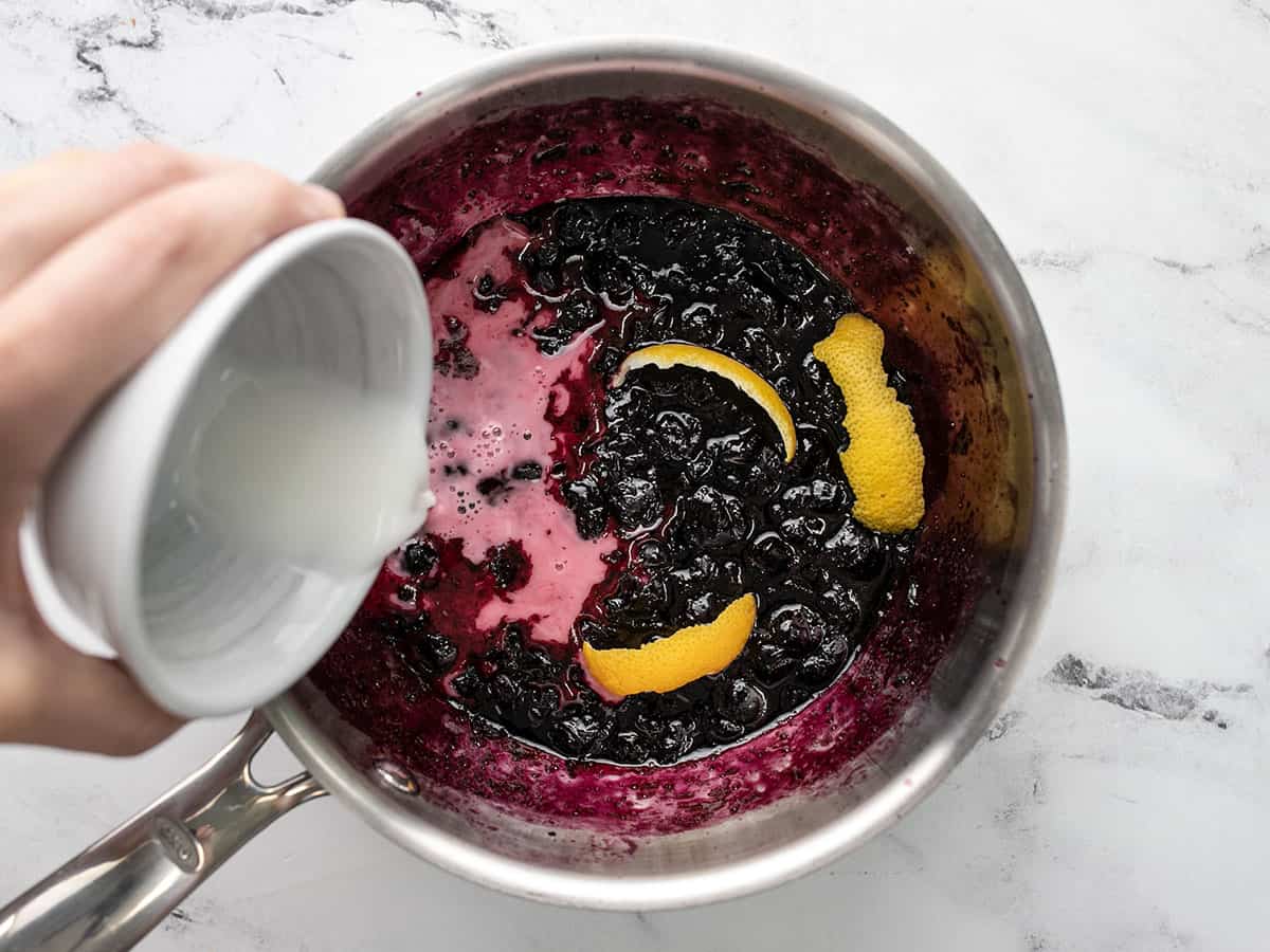 Overhead shot of lemon and cornstarch being added to blueberry sauce.